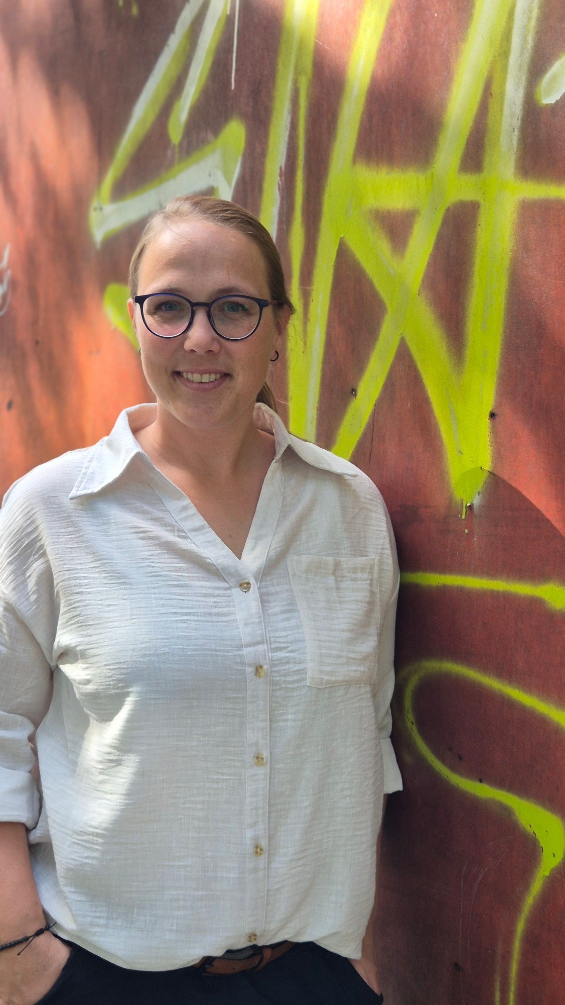 Linda Müller im Portrait vor einer bunten Graffiti-Wand
